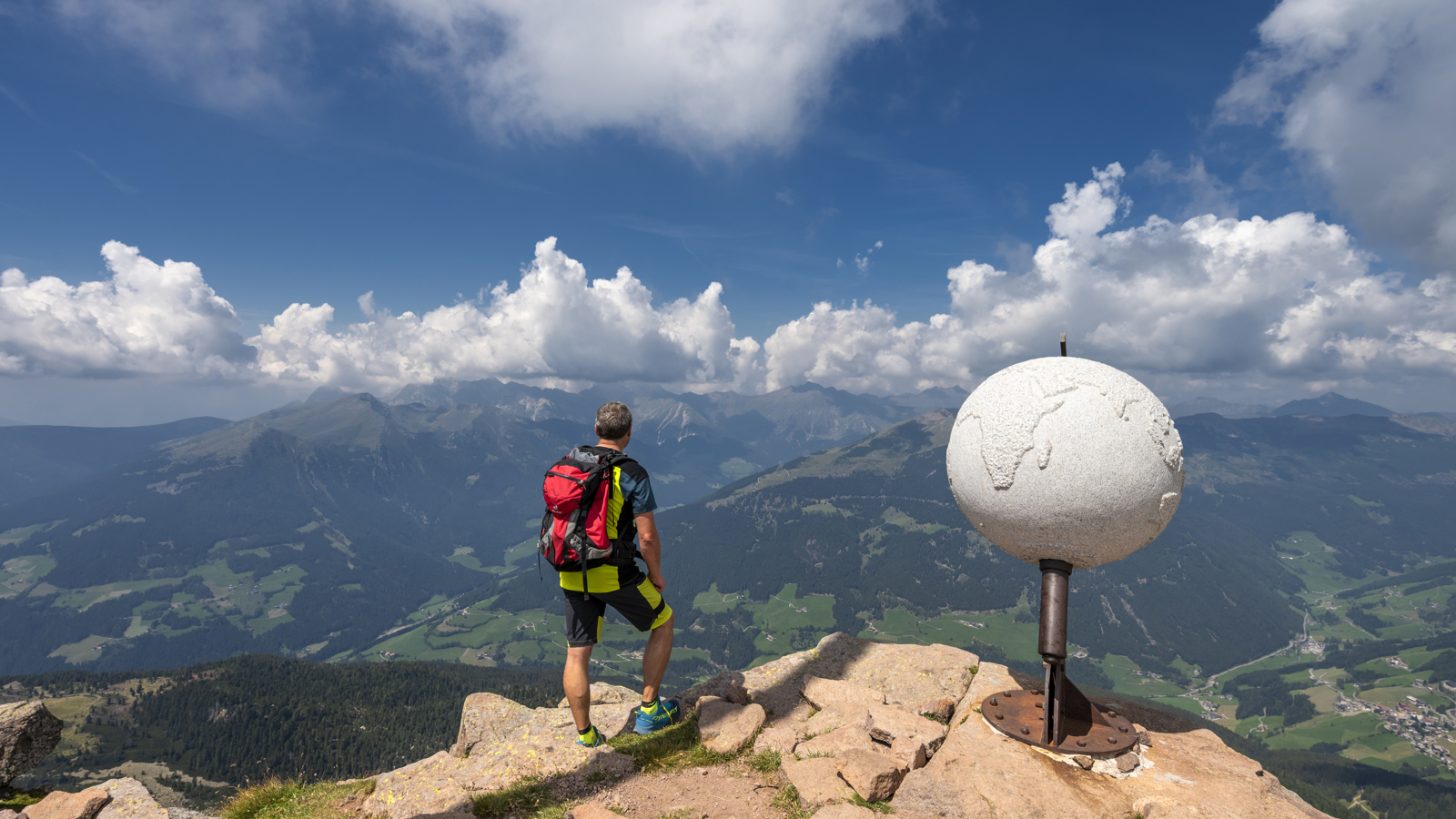 Man die over een landschap uitkijkt met een wereldbol naast zich