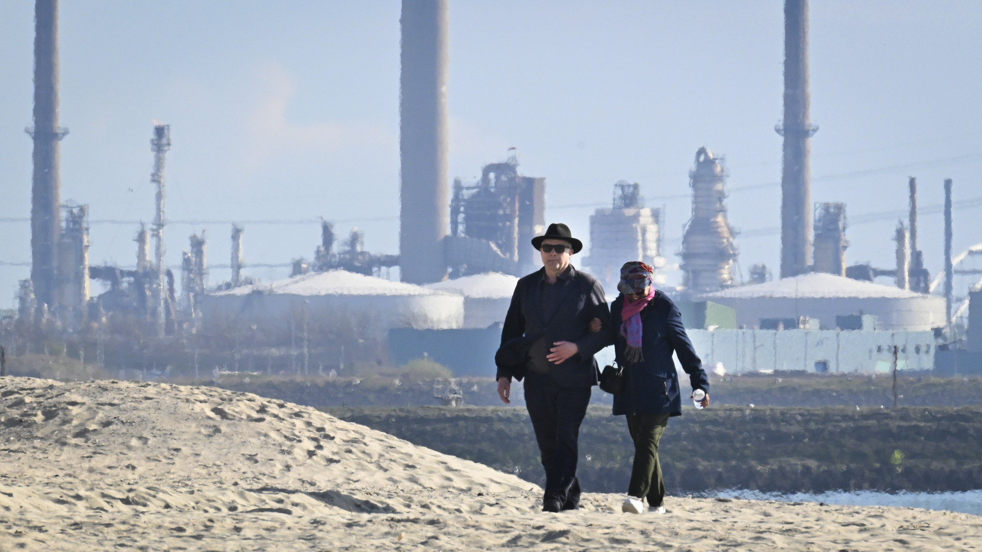 Een ouder stel loopt door de haven van Rotterdam, met de olie industrie bij de Europoort op de achtergrond