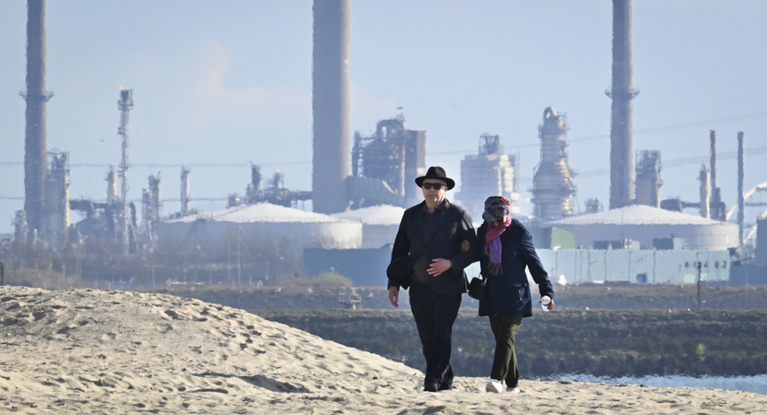 Een ouder stel loopt door de haven van Rotterdam, met de olie industrie bij de Europoort op de achtergrond
