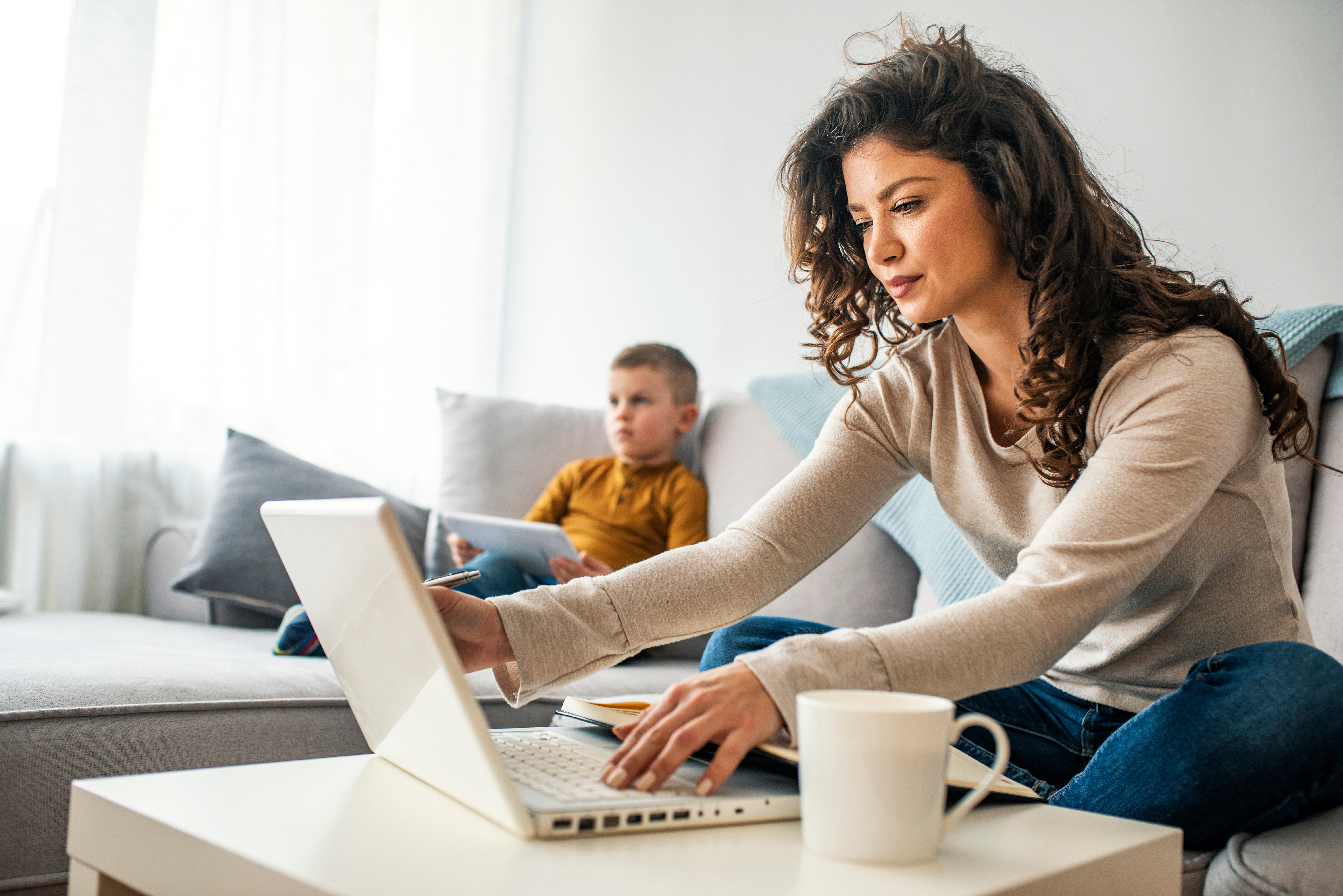 Jonge vrouw achter laptop met kind op bank.