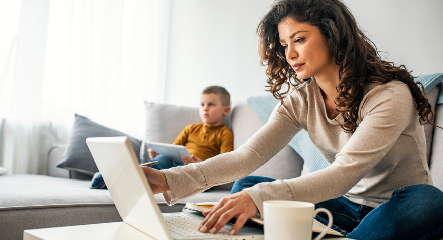 Jonge vrouw achter laptop met kind op bank.