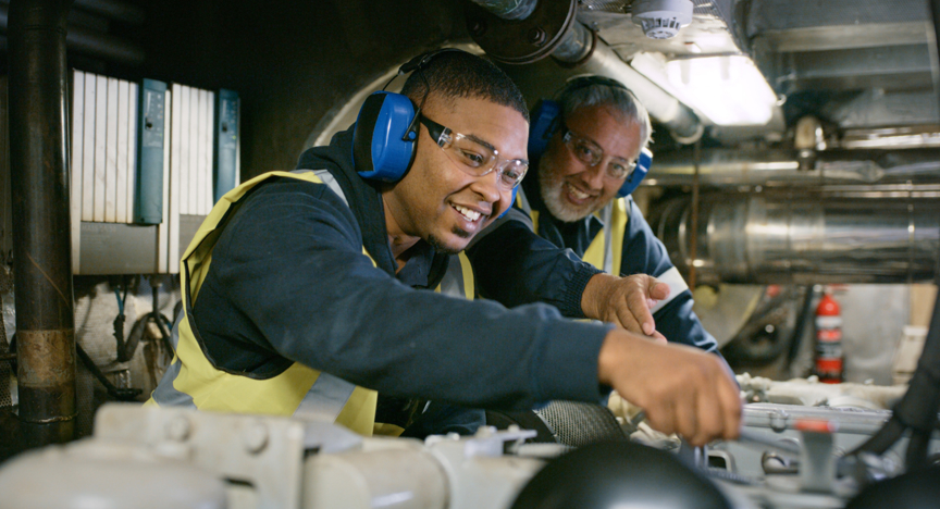 Twee mannen, oud en jong, werken samen aan een machine