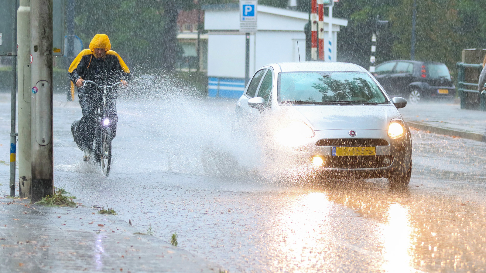Auto rijdt door plas water in de regen en maakt fietser nat