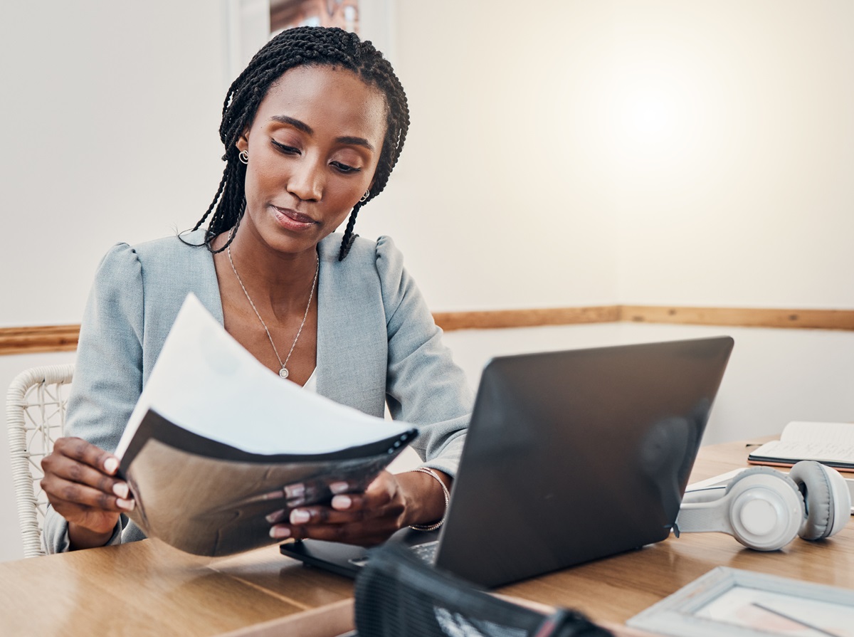 Donkere vrouw met werkdocumenten achter laptop
