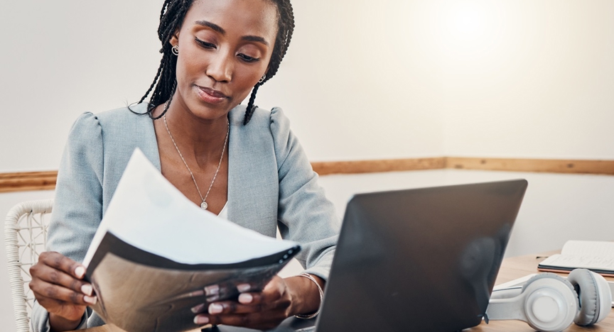 Donkere vrouw met werkdocumenten achter laptop