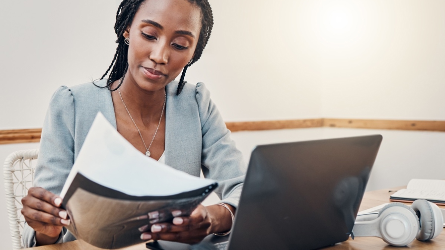 Donkere vrouw met werkdocumenten achter laptop