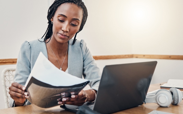 Donkere vrouw met werkdocumenten achter laptop