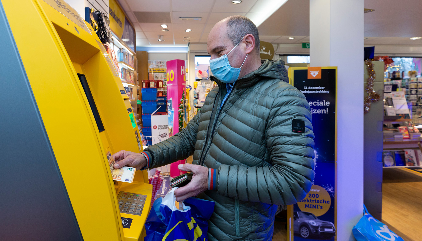 Man neemt geld op bij geldautomaat in winkel Man neemt geld op bij geldautomaat in winkel