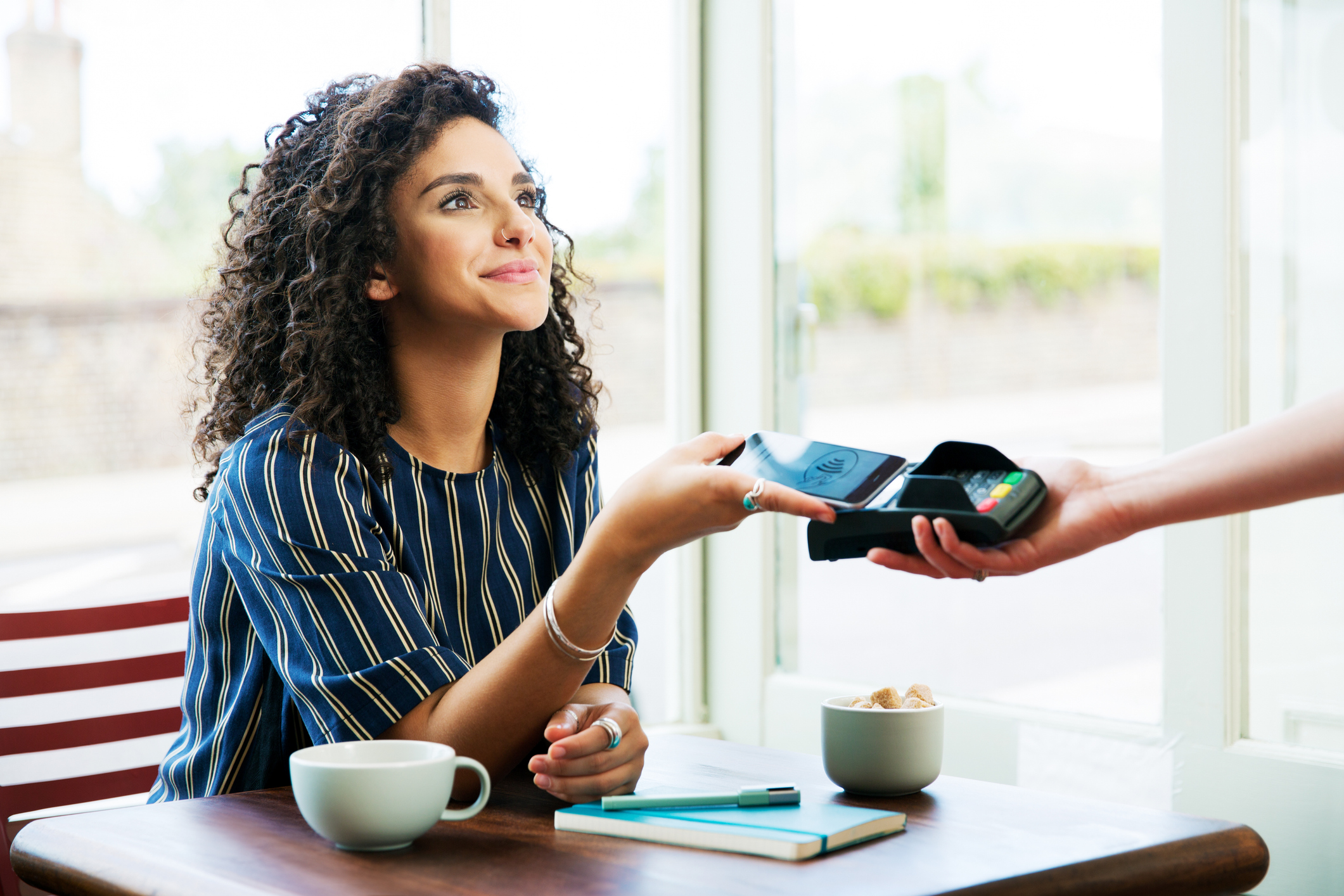 Jonge vrouw gebruikt mobiele telefoon om koffie af te rekenen.