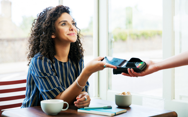 Jonge vrouw gebruikt mobiele telefoon om koffie af te rekenen.