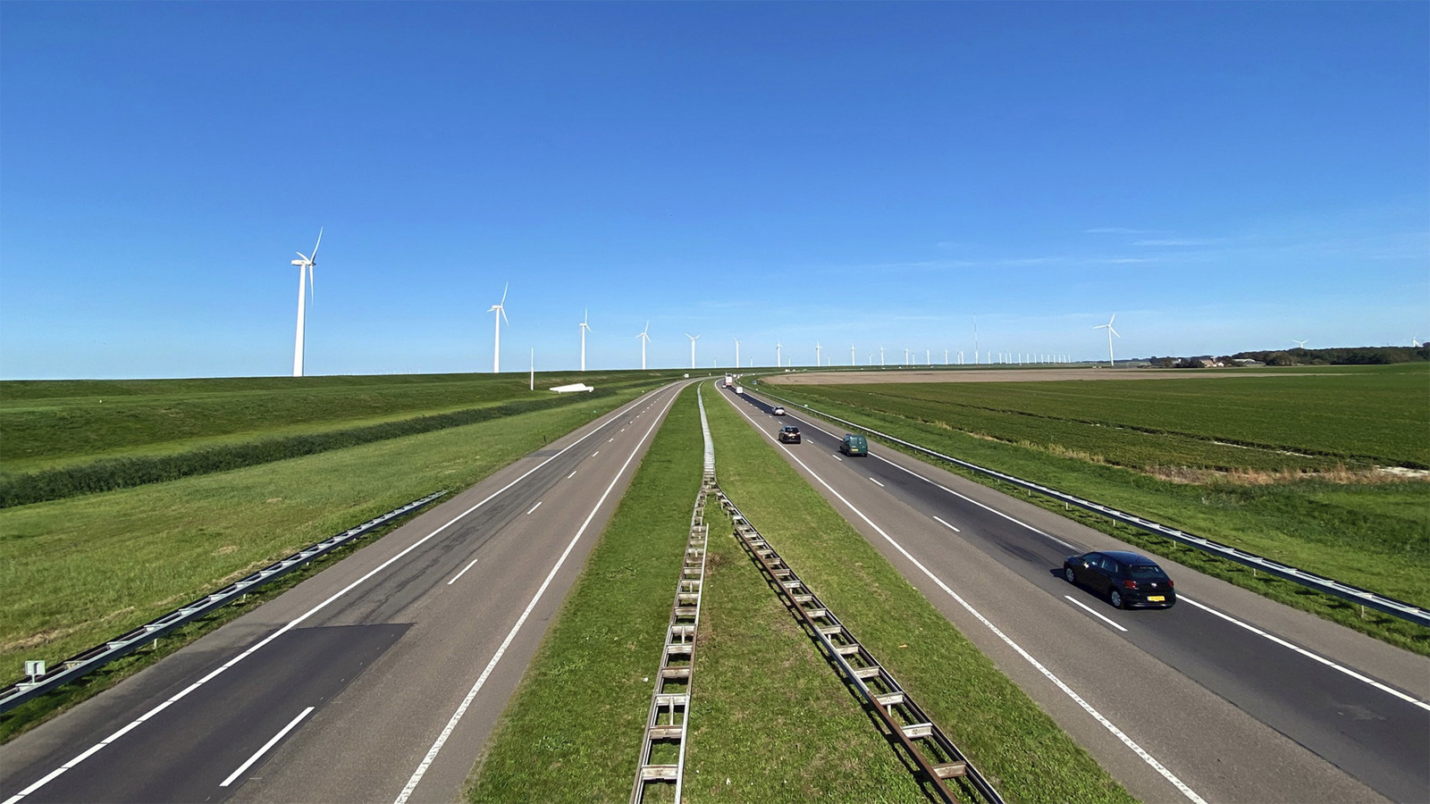 Een paar auto's op een snelweg met windmolens in de verte