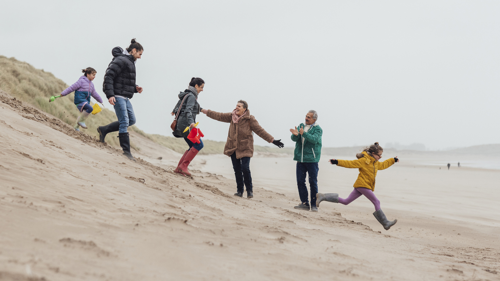 Familie van verschillende generatie’s rent van een duin af op het strand