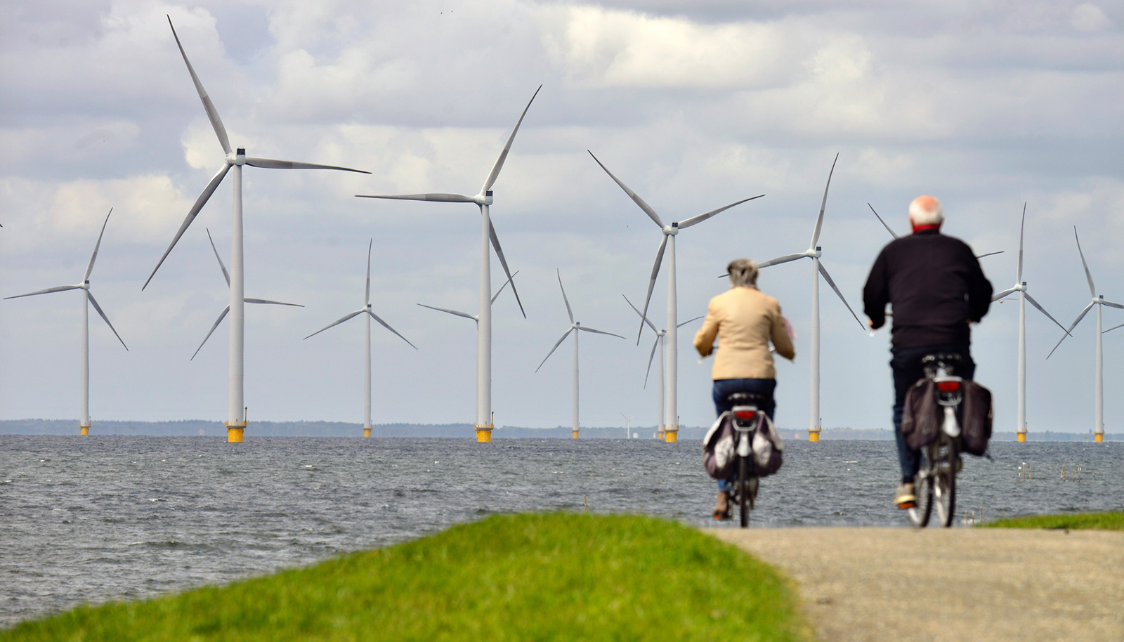 Mensen die fietsen bij de zee met windmolens in het water