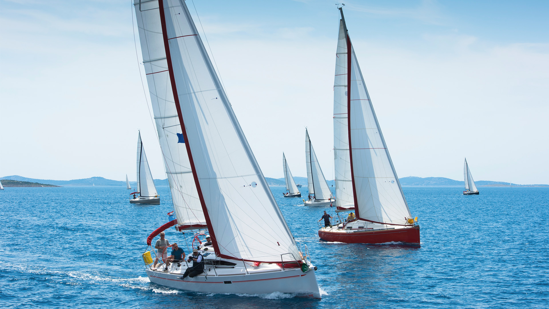 Groep zeilboten vaart samen over open water onder heldere lucht