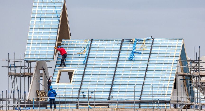 Bouwvakkers plaatsen dakdelen op een woning in aanbouw.