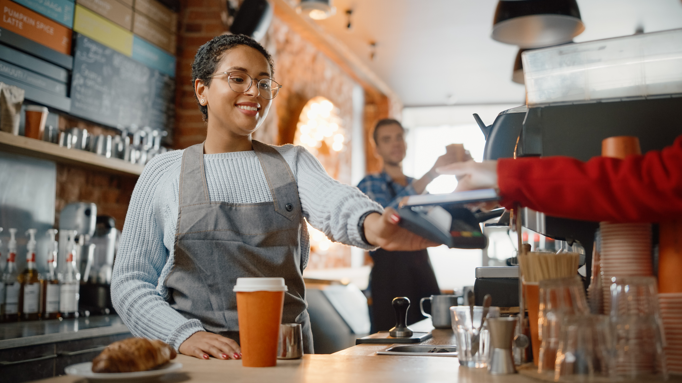 Klant gebruikt mobiel om te betalen voor Take Away Latte en Croissant naar een Barista in koffiebar.