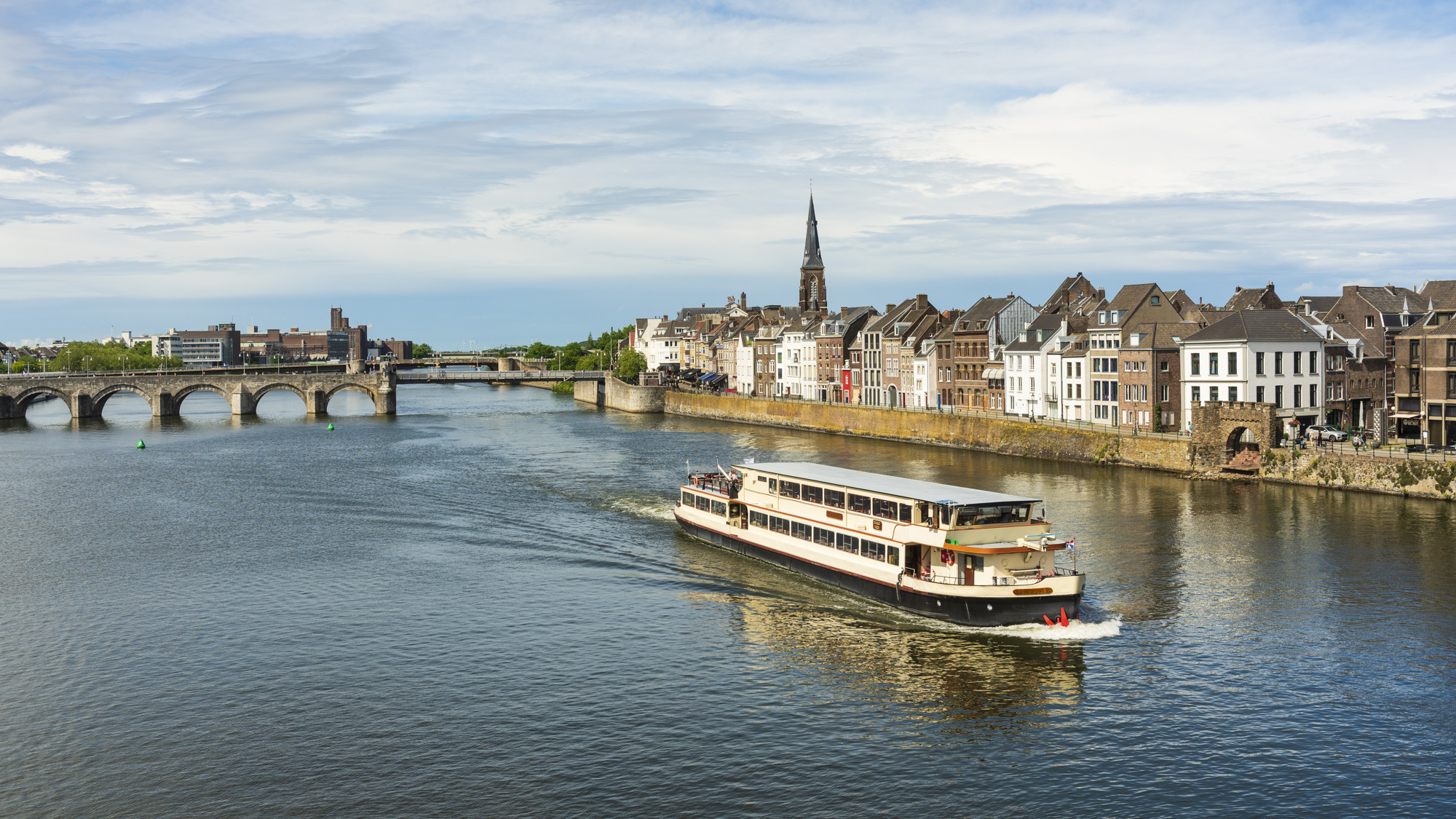De rechter Maasoever met het stadsdeel Wijck en uizticht over de rivier waar een rondvaartboot vaart.