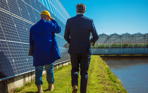 Twee mannelijke ingenieurs lopen langs een rij kassen met zonnepanelen.