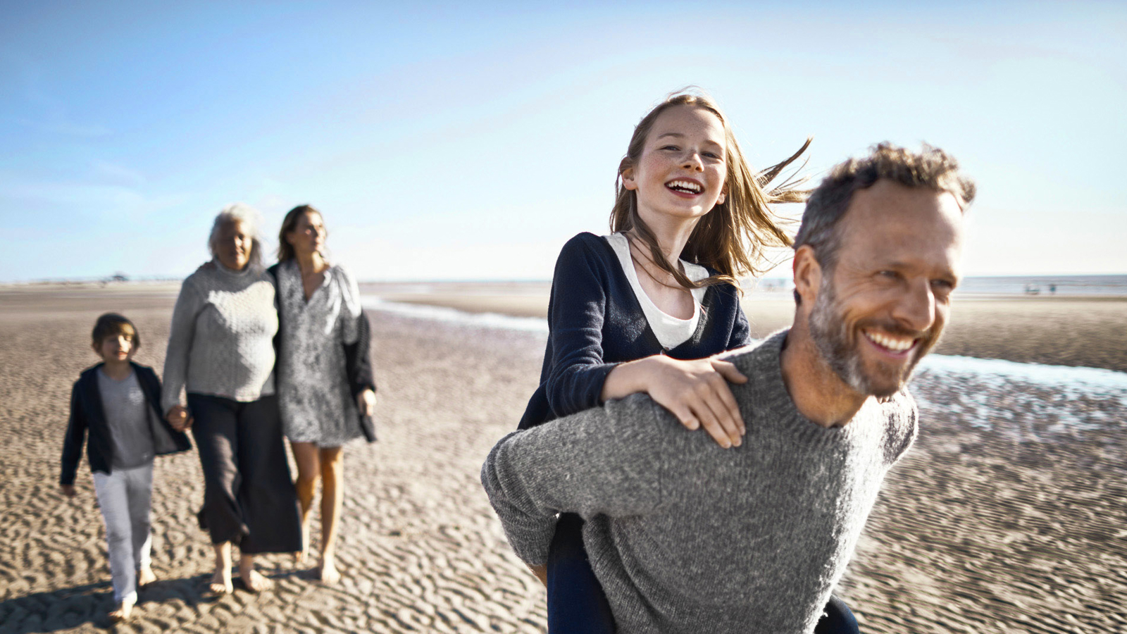 Een gezin op het strand met een man die een kind op zijn rug draagt