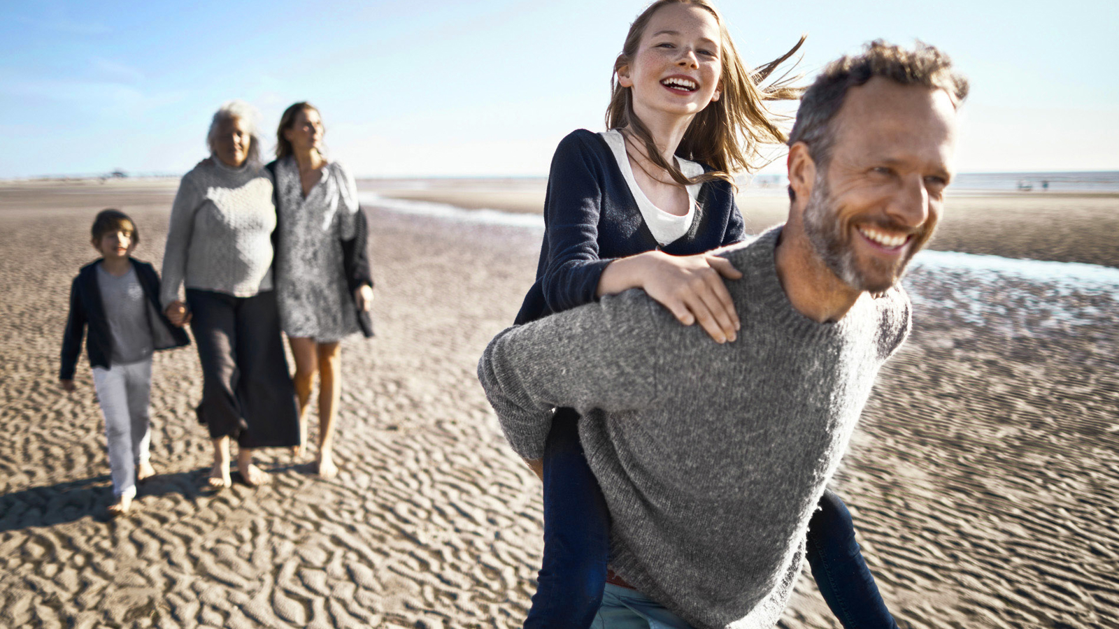 Een gezin op het strand met een man die een kind op zijn rug draagt