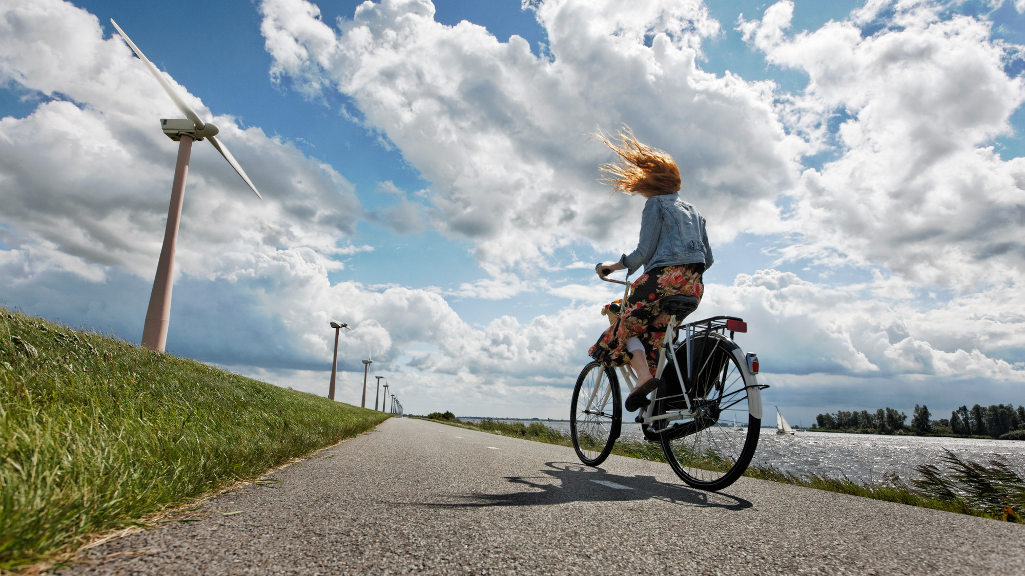Vrouw fietst met tegenwind langs een kanaal.