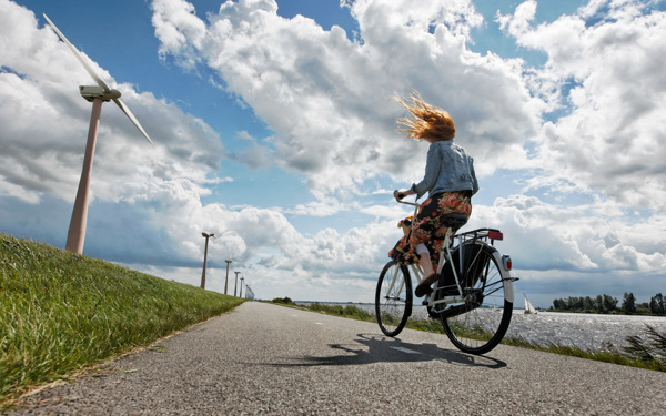 Vrouw fietst met tegenwind langs een kanaal.
