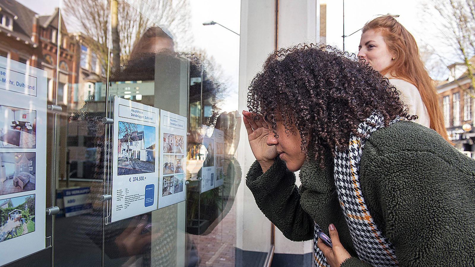 Vrouw kijkt door raam bij makelaar naar een koophuis