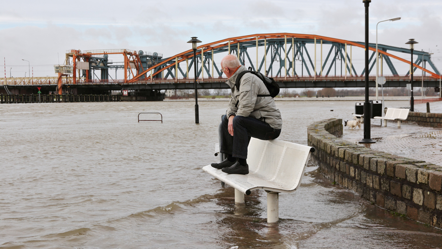 Oudere man houdt zijn voeten droog op een bankje in de overstromende Ijssel van Zutphen 