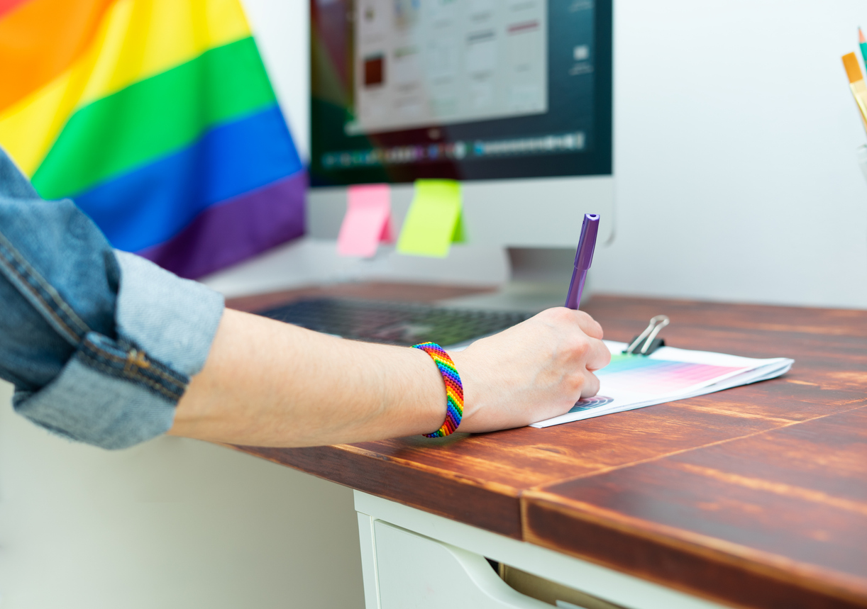 Vrouwenarm achter computer met Pride vlag op achtergrond 