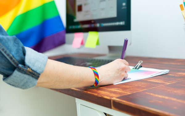 Vrouwenarm achter computer met Pride vlag op achtergrond 