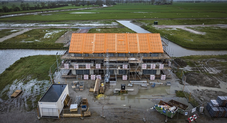 Dronefoto van een nieuwbouwhuis in aanbouw met lege kavels op de achtergrond