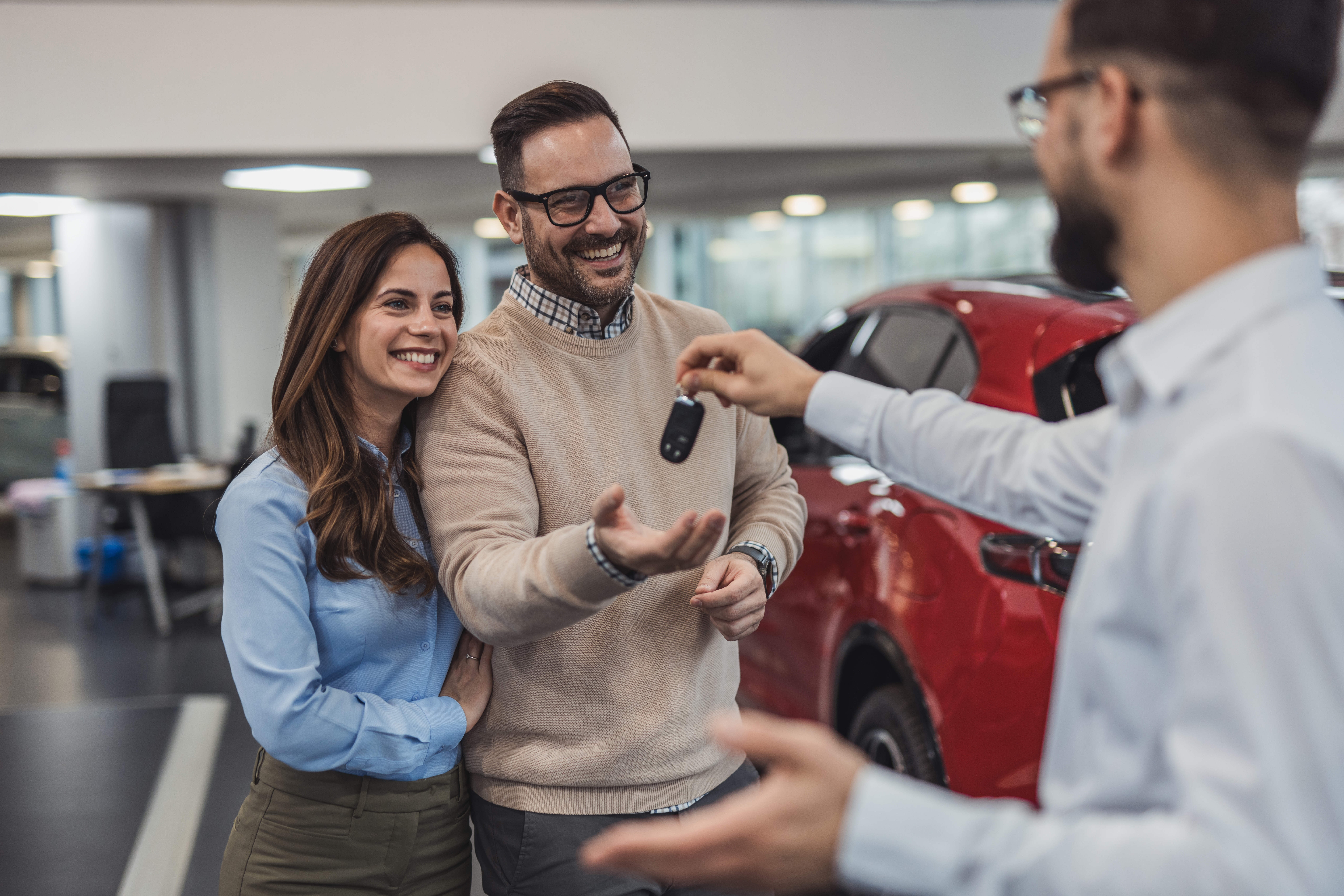 Stel ontvangt de sleutels van hun nieuwe rode auto van een autoverkoper in een showroom.