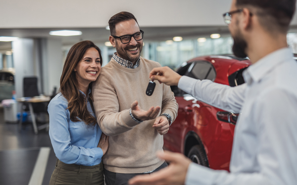 Stel ontvangt de sleutels van hun nieuwe rode auto van een autoverkoper in een showroom.
