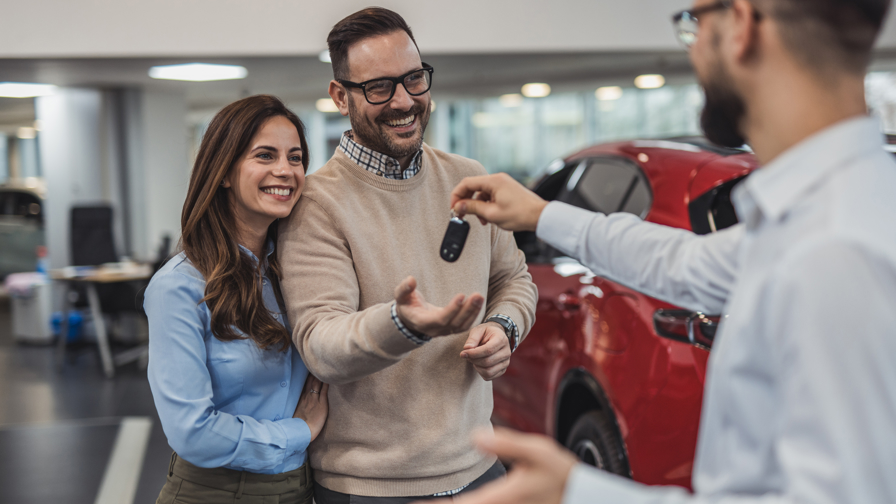 Stel ontvangt de sleutels van hun nieuwe rode auto van een autoverkoper in een showroom.