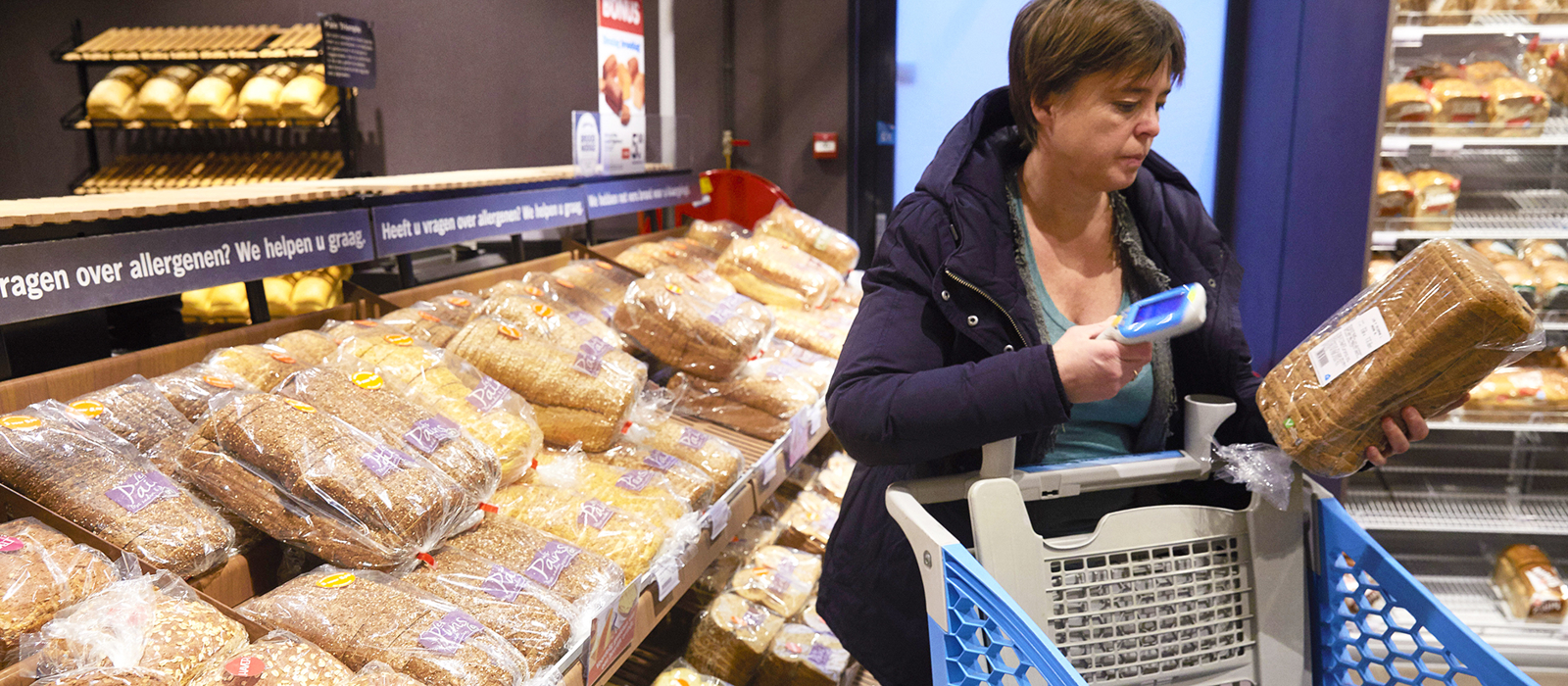 Vrouw scant brood met zelfscanner in supermarkt