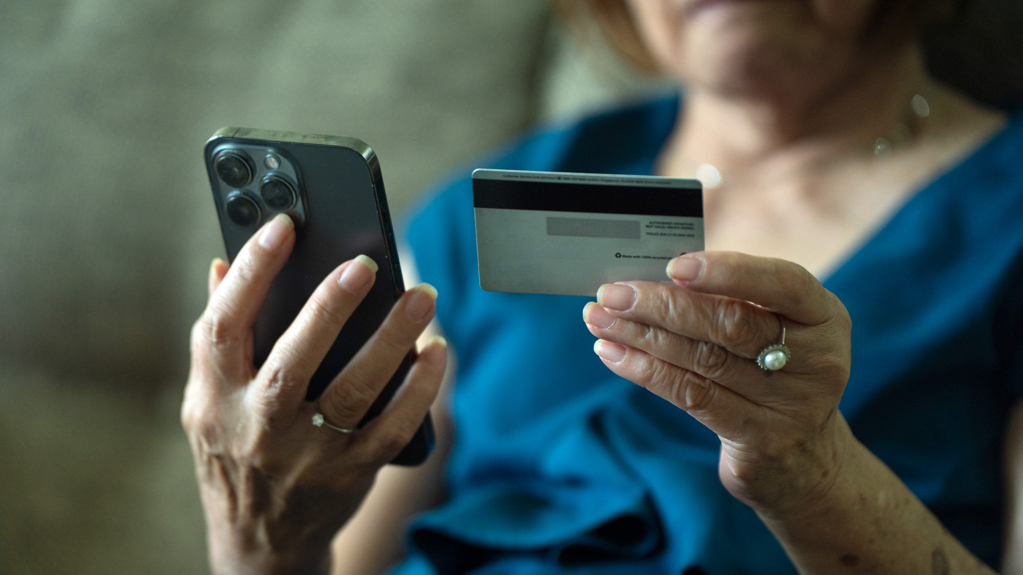 Een oudere vrouw kijkt naar haar creditcard en telefoon.